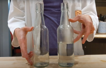An Educator indicates the water levels in two glass bottles with their hands.