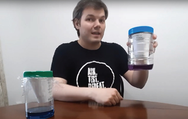 An Educator holds up a jar containing a purple liquid.