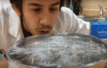 An Educator blow salt grains that are sitting on top of a plastic film stretched across top of a pot.