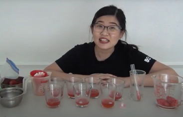 An Educator sits behind several glass dishes containing a red liquid.