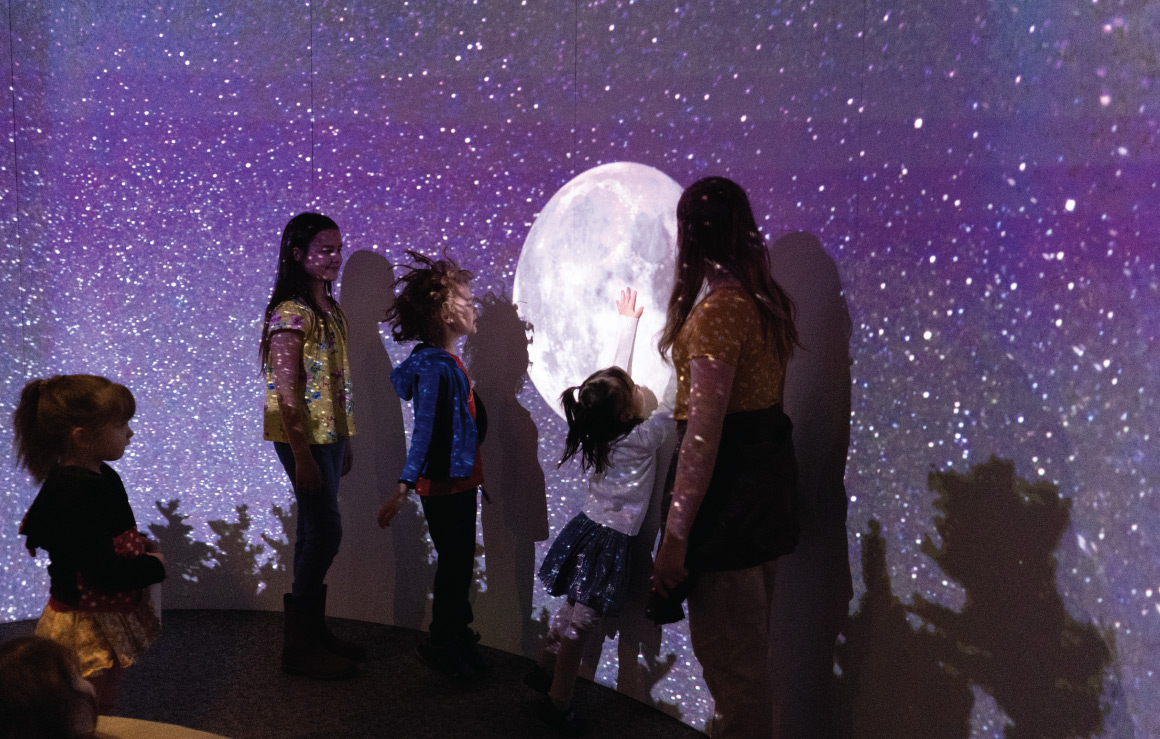 Children interact with a wall projection of the moon and stars.