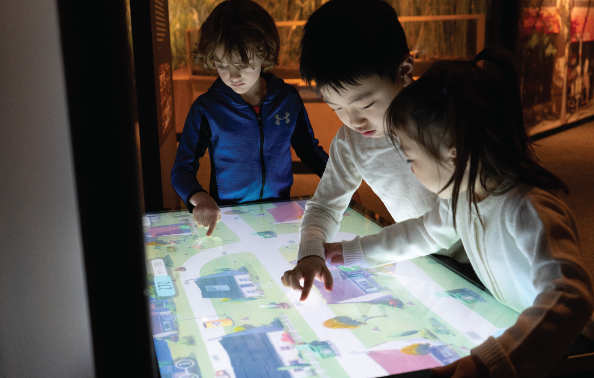 Three children interact with a touch screen.