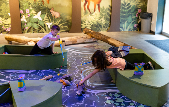 Two kids sitting inside two separate boats and catching toy fishes with a fishing rod.