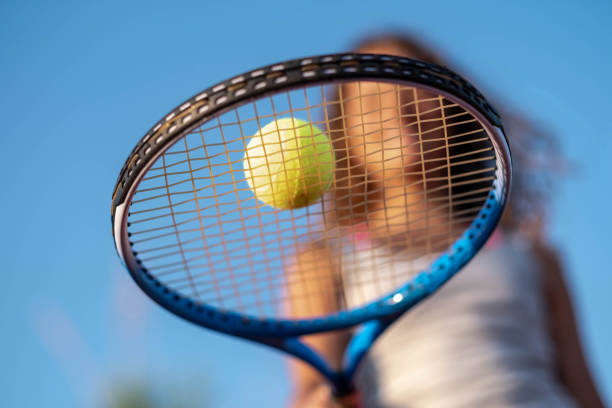A girl balances a tennis ball on a tennis racket.