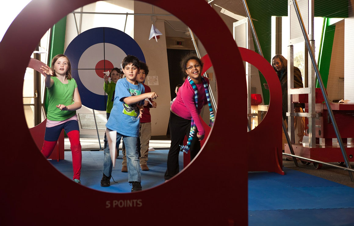 Children throw paper airplanes through targets.