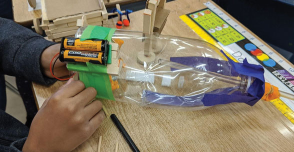 A student works on a home made science experiment involving batteries and a plastic bottle.