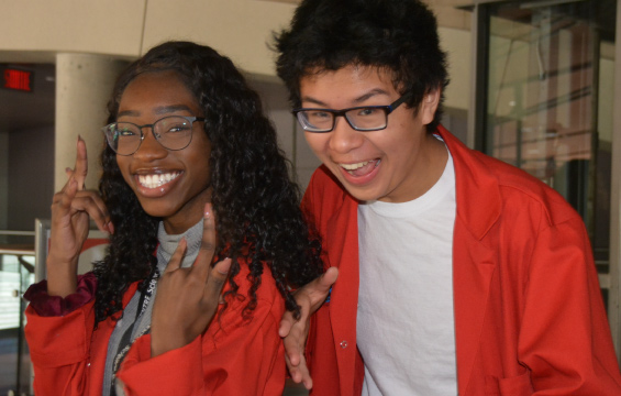 Two smiling Science School students pose together in their red lab coats