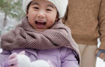 A girl holds snowballs while dressed for winter.