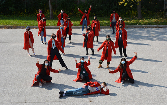 Science School students wearing red lab coats and face masks pose for a photo outside