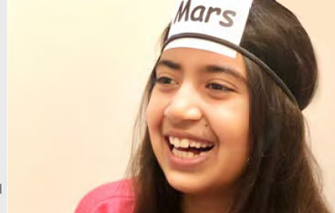 A child smiles while wearing a headband with the word Mars on it.