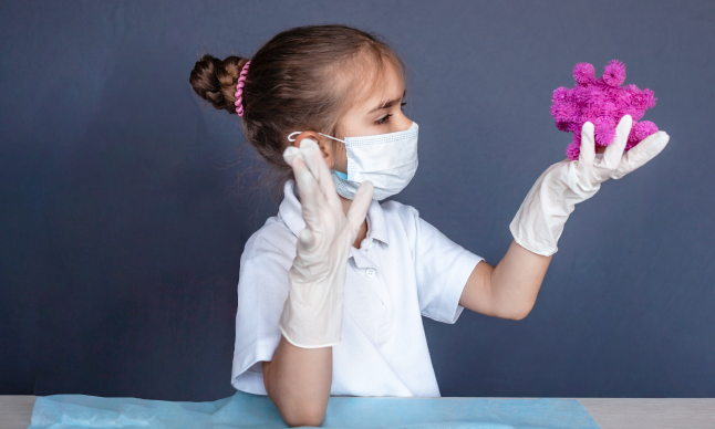 A girl in PPE holding a large toy virus.