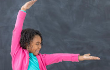 A girl holds her arms out in front of a blackboard.