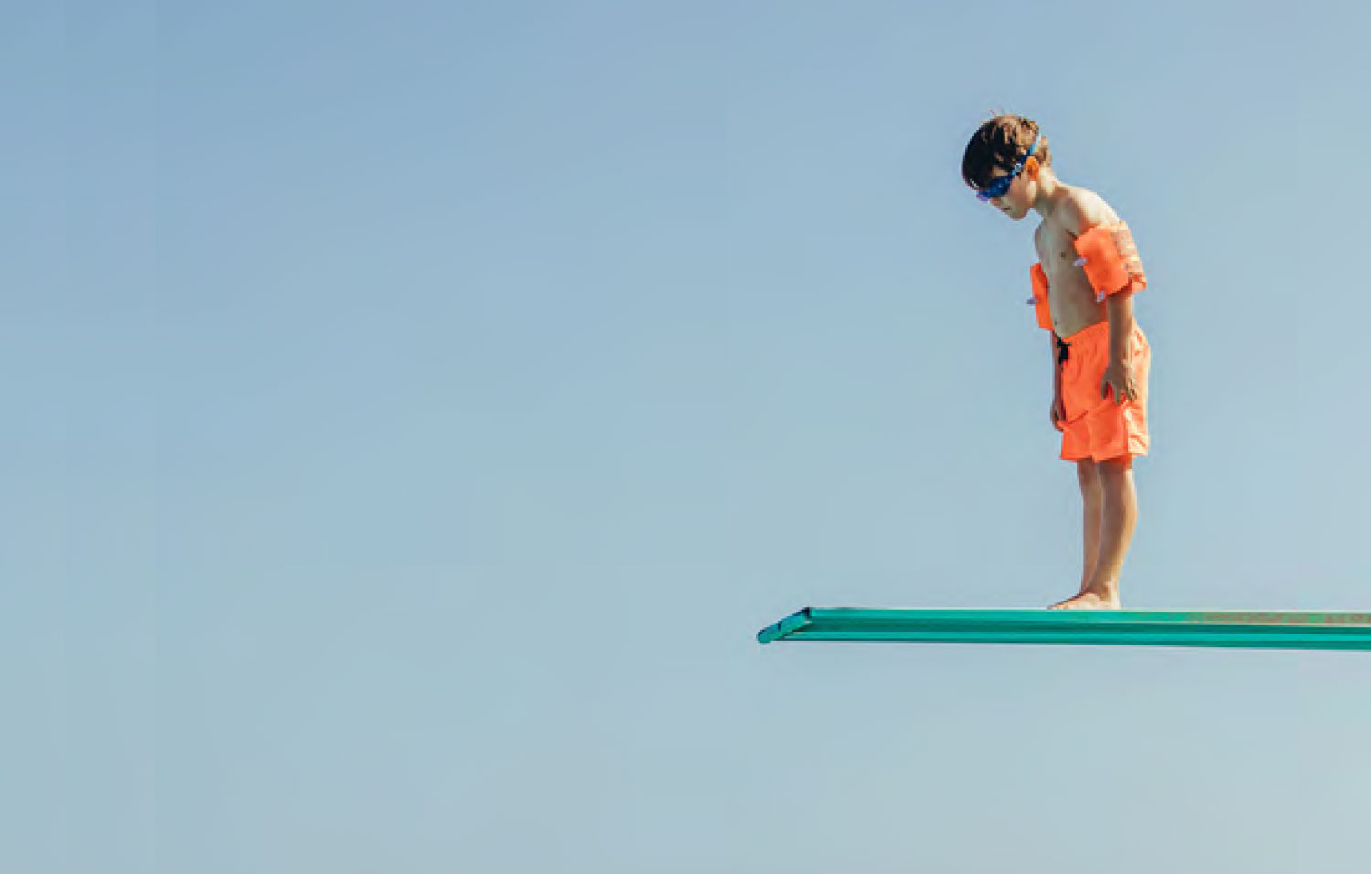 A young boy stands on a diving board looking down.