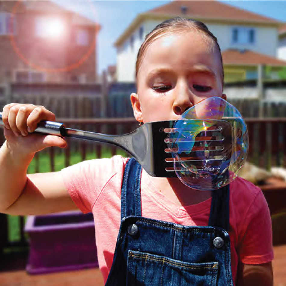 A child blows multiple bubbles with a slotted spatula.