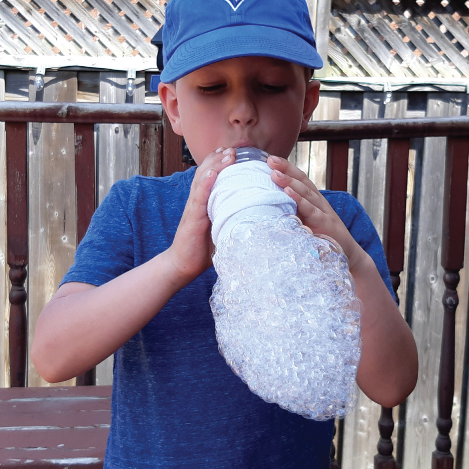 A child blows multiple bubbles through a sock, creating a bubble foam.