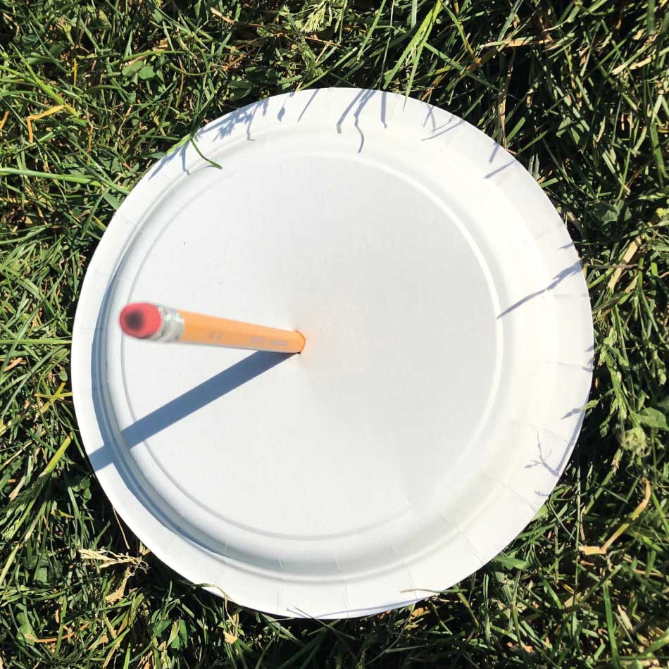 An upright pencil poked into the centre of a paper plate casts its shadow onto the plate.