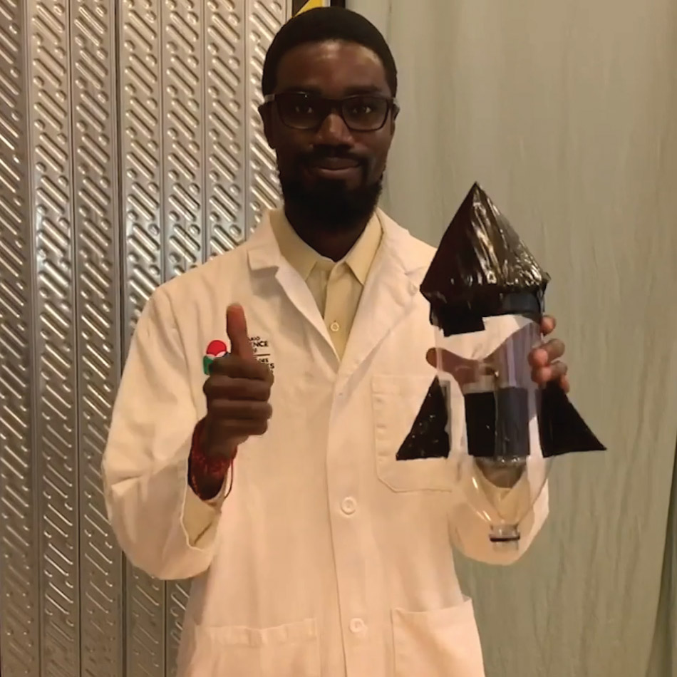 A host wearing a white lab coat holds up a completed rocket and gives a thumbs up.