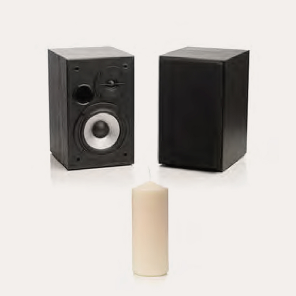 Two speakers sit on the floor or a table facing each other, with a candle set up in between them.