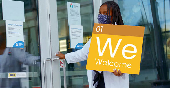 A woman with a face mask holds a welcome sign at the Science Centre