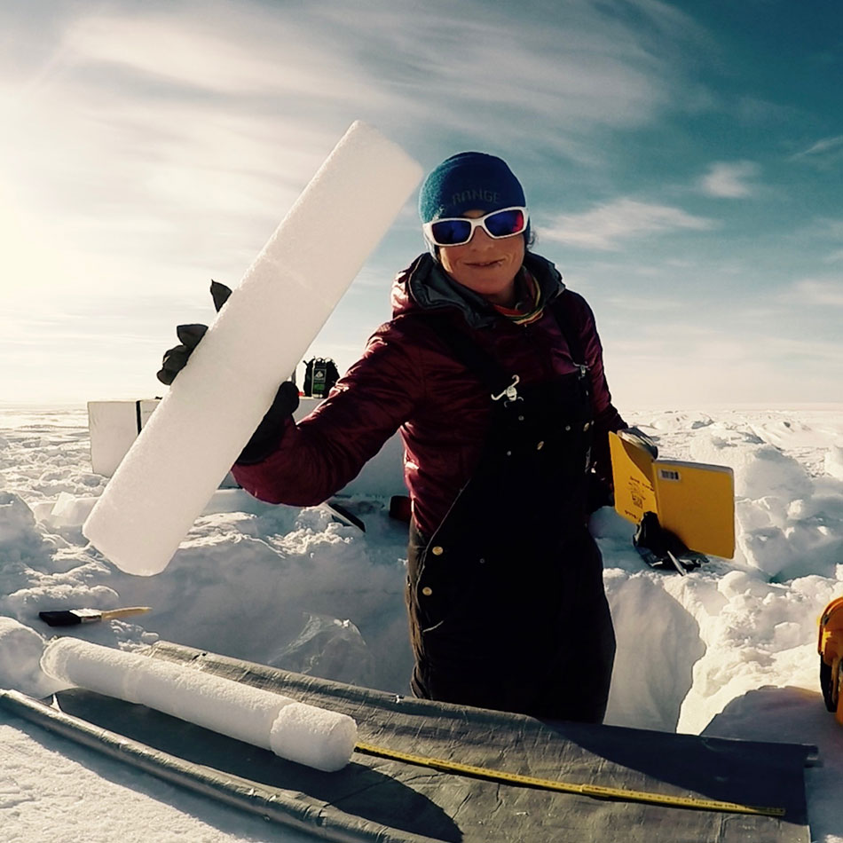 A woman in snow gear holds an ice core sample.