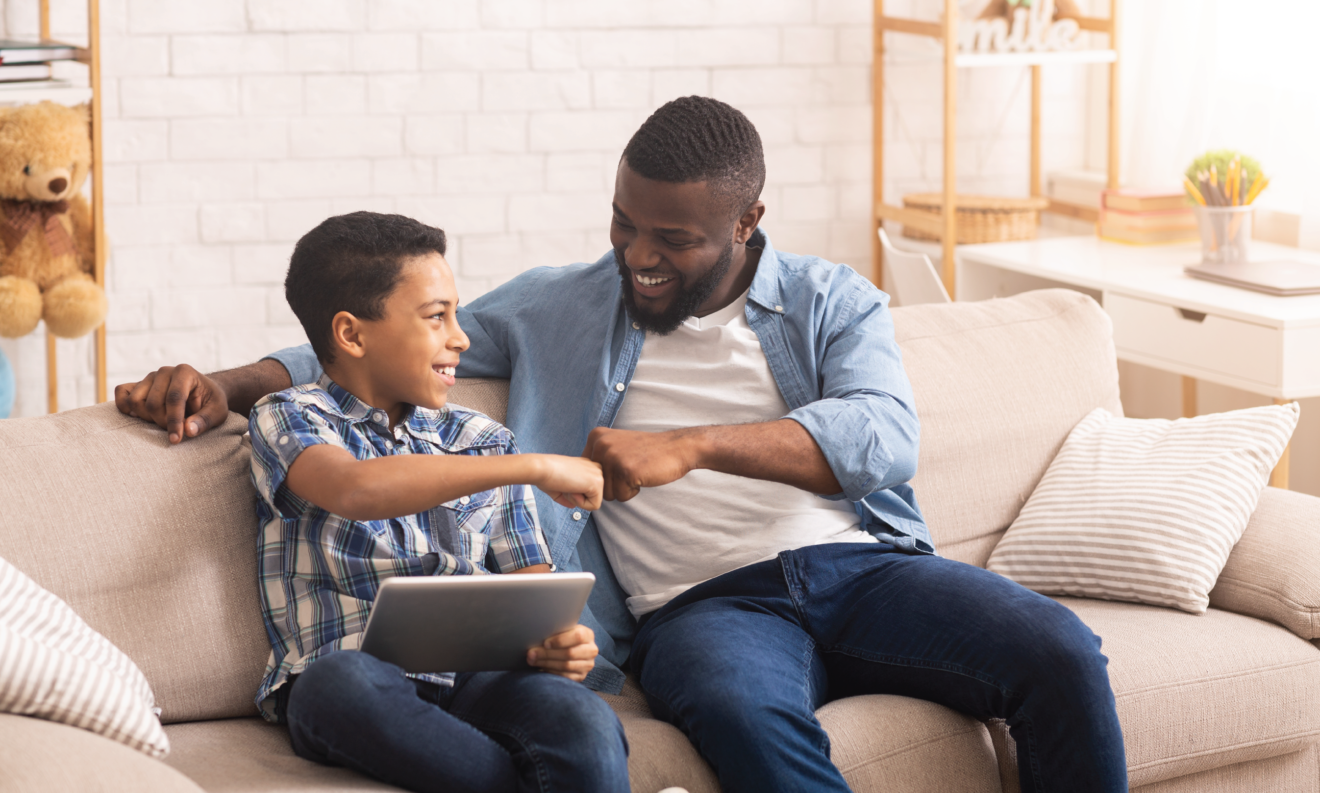 A man and boy bump fists while using a tablet.