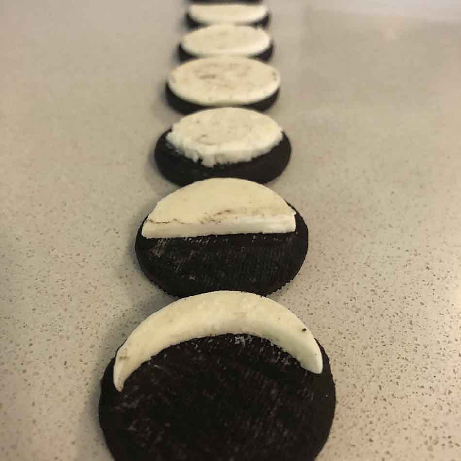 Sandwich cookies are laid out in a row, with their cream centres carved away to look like different phases of the moon.
