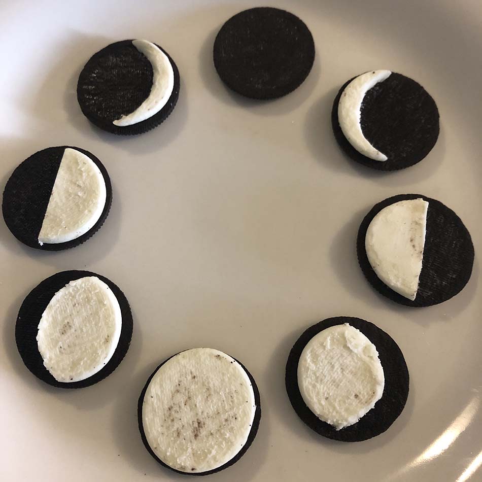 Sandwich cookies are laid out on a plate in a circle, with their cream centres carved away to look like different phases of the moon.