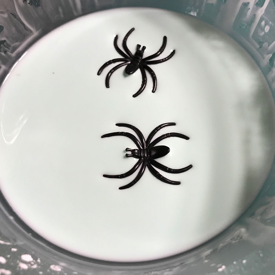 Two black toy spiders sit in a bowl of white Oobleck.