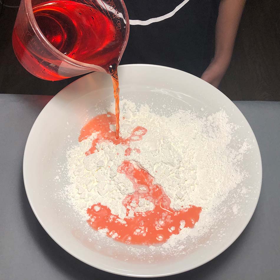 Water coloured red with food colouring is poured into a dish containing cornstarch.
