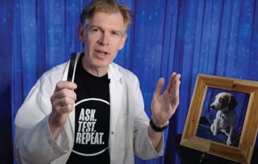 An Educator holds up a magnifying glass, sitting next to a framed photo of a beagle.