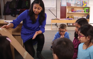 A teacher shows students a ramp made of cardboard.