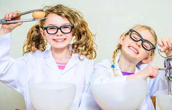 Two young girls in lab coats using kitchen tools to make ice cream.