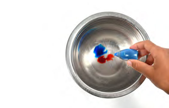 A hand squeezing drops of colour into a bowl of water.