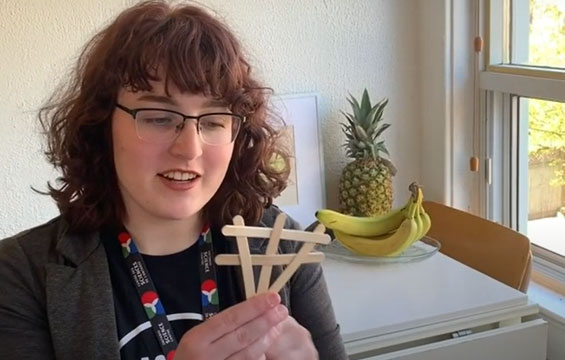 A Science Centre host holding popsicle sticks.