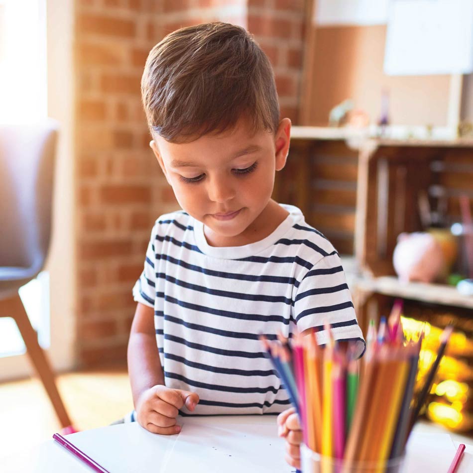 A young child colours with coloured pencils.