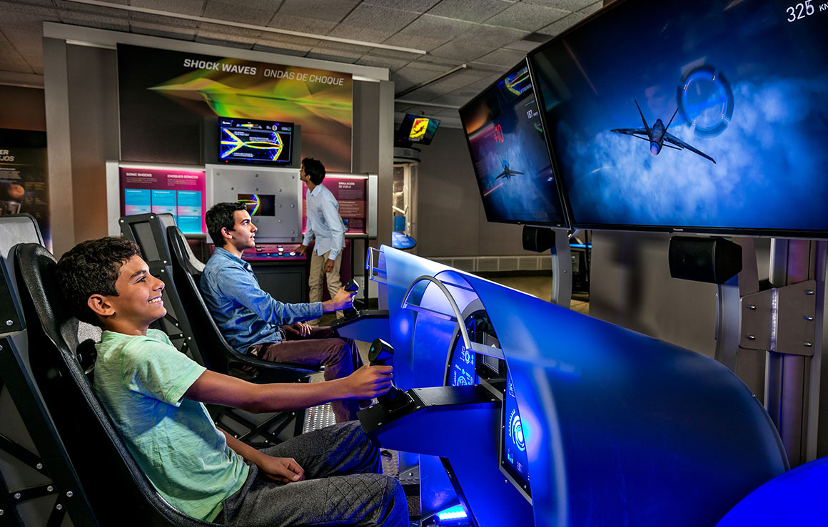 A man and a boy sitting in immersive pods using a flight simulator.