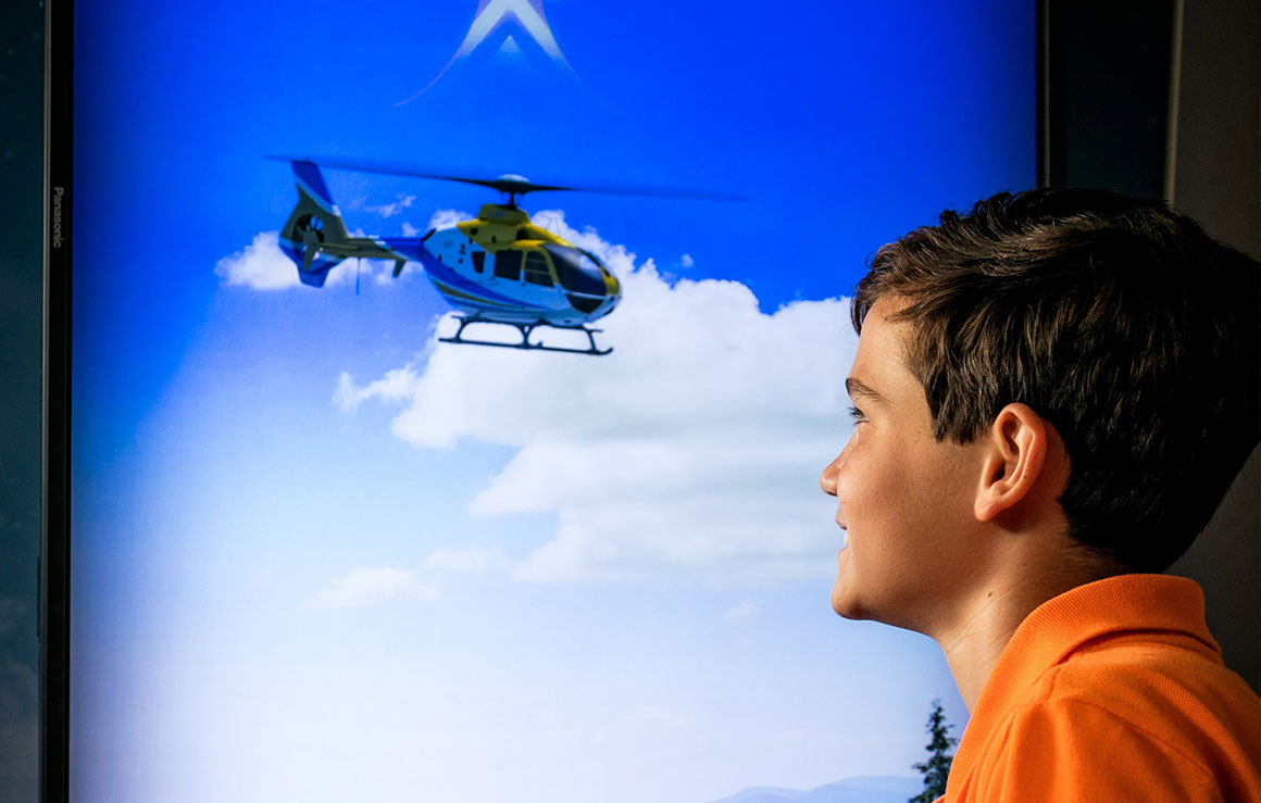 A boy watches a screen with a helicopter on it.