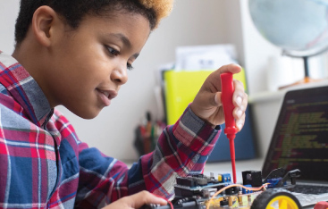 A young Black child works on a motorized vehicle with a screwdriver.