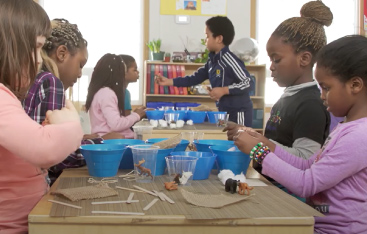 Several young students work together and build with popsicle sticks.