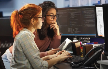 Two young women work together at a computer.