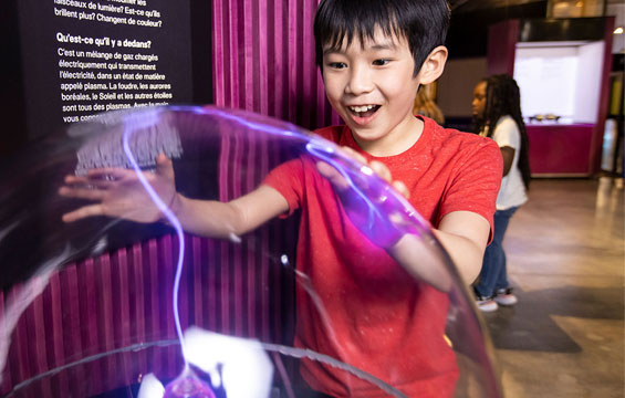 A boy places his hands on a plasma ball.