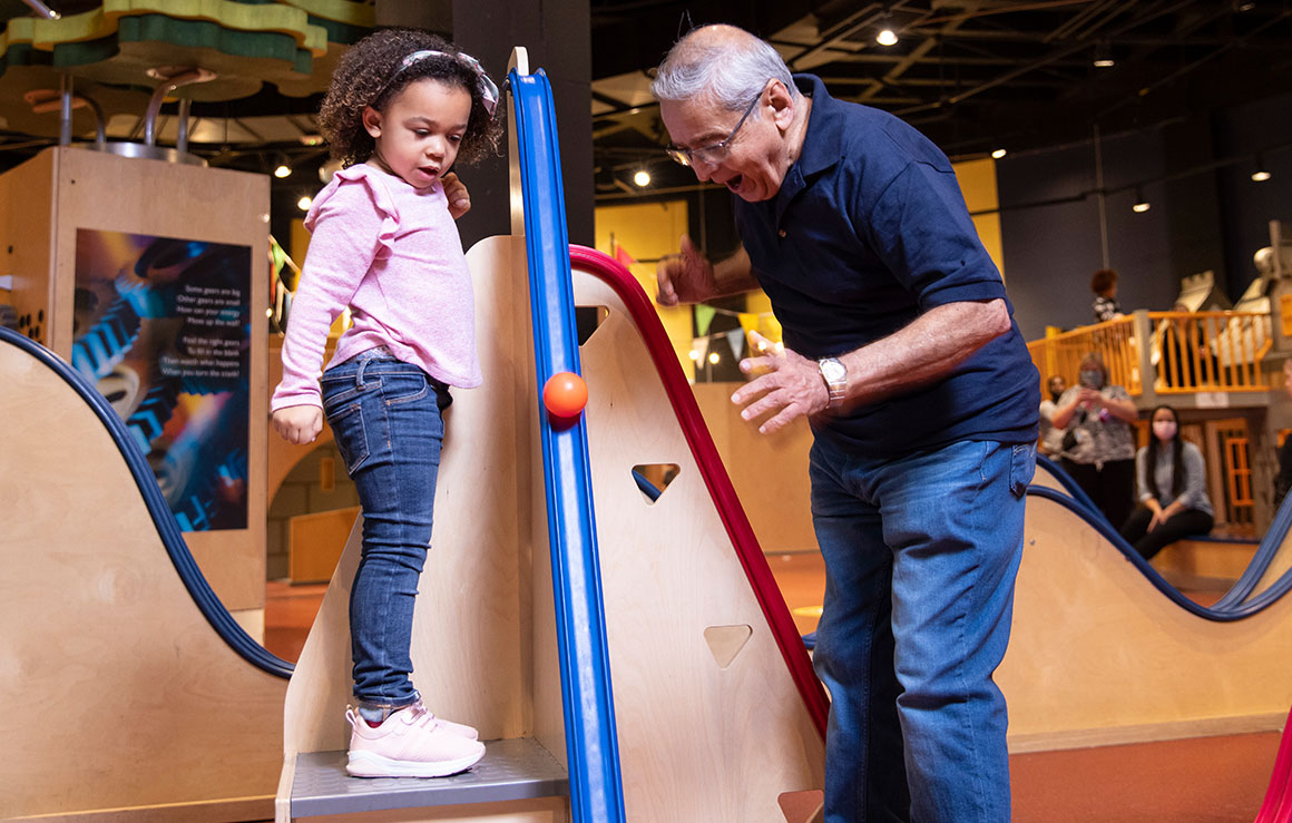 A girl and a man rolling a ball down a ramp.