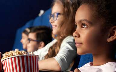 Children watching a movie while holding popcorn.