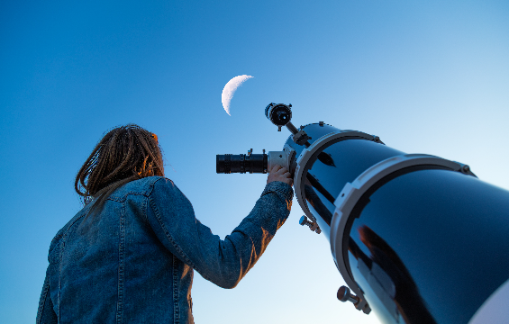 a girl looking through a telescope at the Moon.