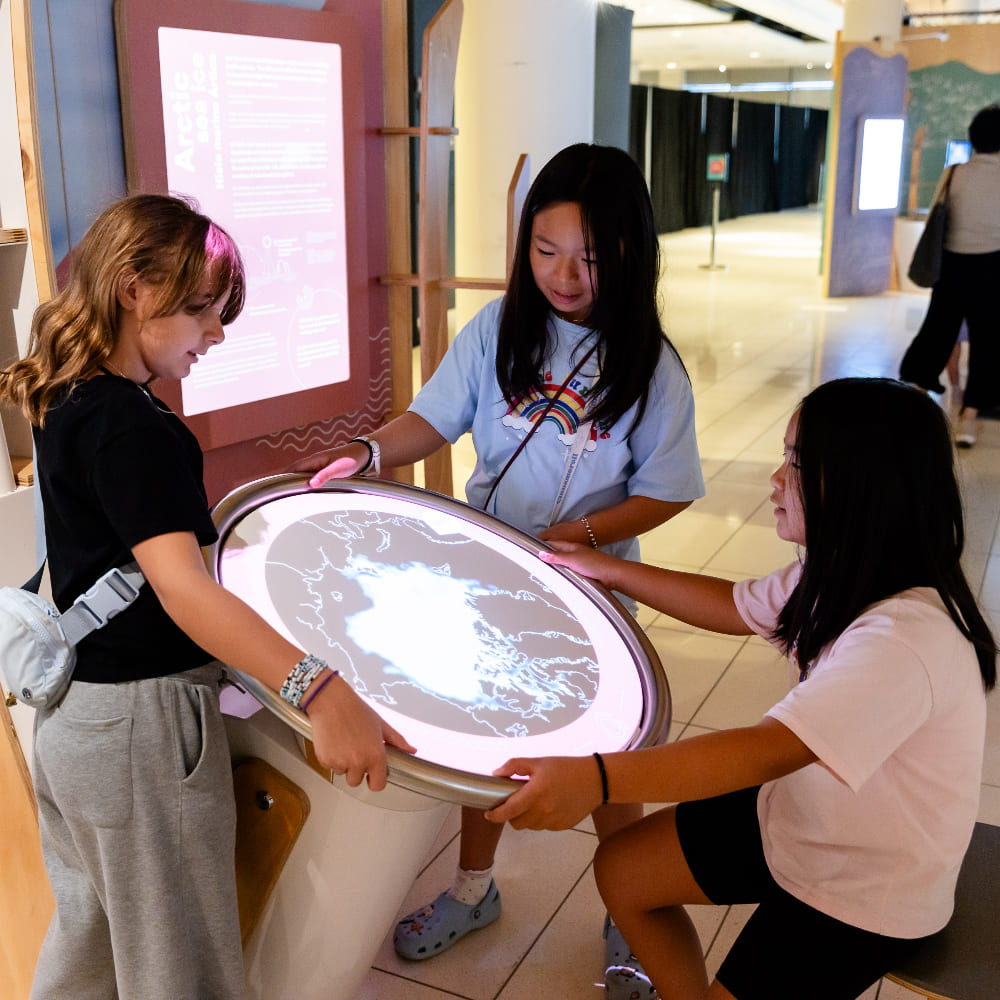 A group of three girls rotating the map to see how seasons change all over the world.