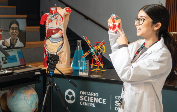 An educator presents to a camera, holding a model human heart.