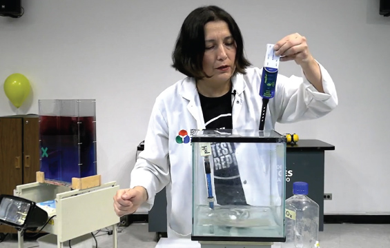 An educator positions a thermometer in a small tank of water