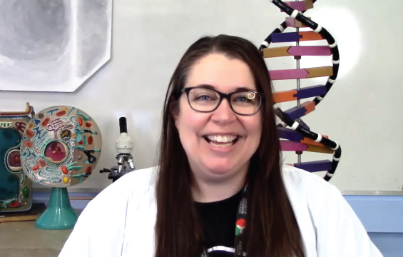 A smiling educator  presents in front of a microscope,  a model of DNA and models of a plant and animal cell