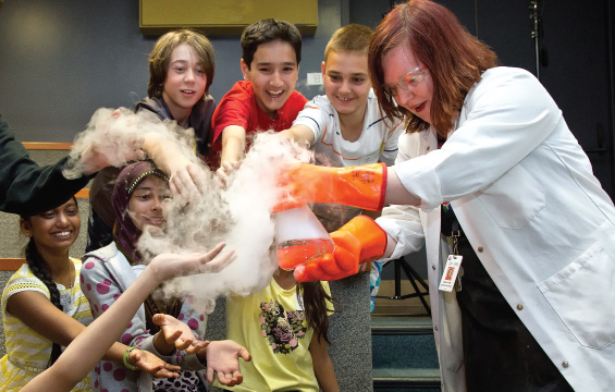 An educator holds out a smoking beaker to a group of students for inspection.