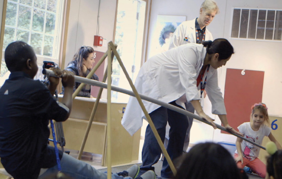 An educator assists a student using a large lever to lift another student.